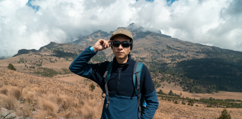 A hiker in the countryside wearing a cap and sunglasses.